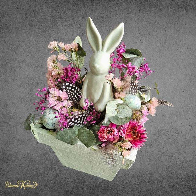 Elegantes Ostergesteck mit dekorativem Hasen, frischen Blumen, Eukalyptus, Federn und Ostereiern in zarten Frühlingsfarben