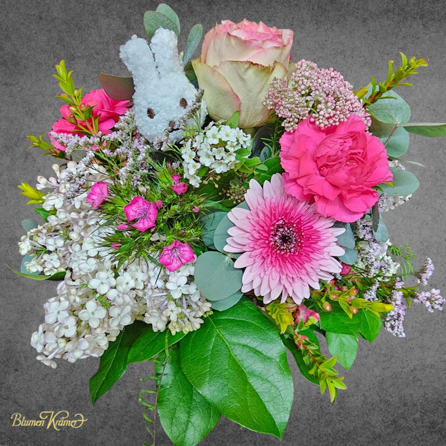 Osterstrauss mit rosa Rosen, Gerbera, Nelken, Flieder und Hasenkopf-Dekoration in frischen Frühlingsfarben