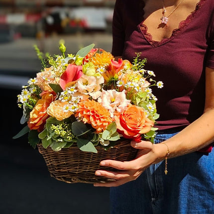 Farbenfroher Blumenkorb mit orangefarbenen Dahlien, Rosen, Nelken und frischen saisonalen Blumen