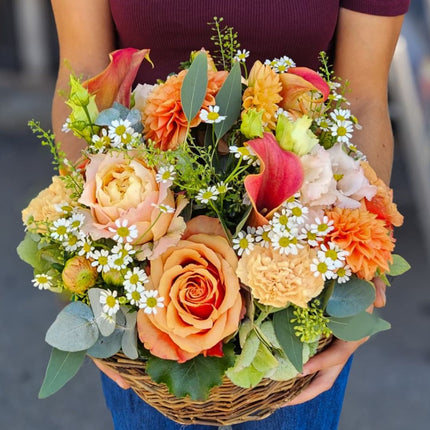 Farbenfroher Blumenkorb mit orangefarbenen Dahlien, Rosen, Nelken und frischen saisonalen Blumen
